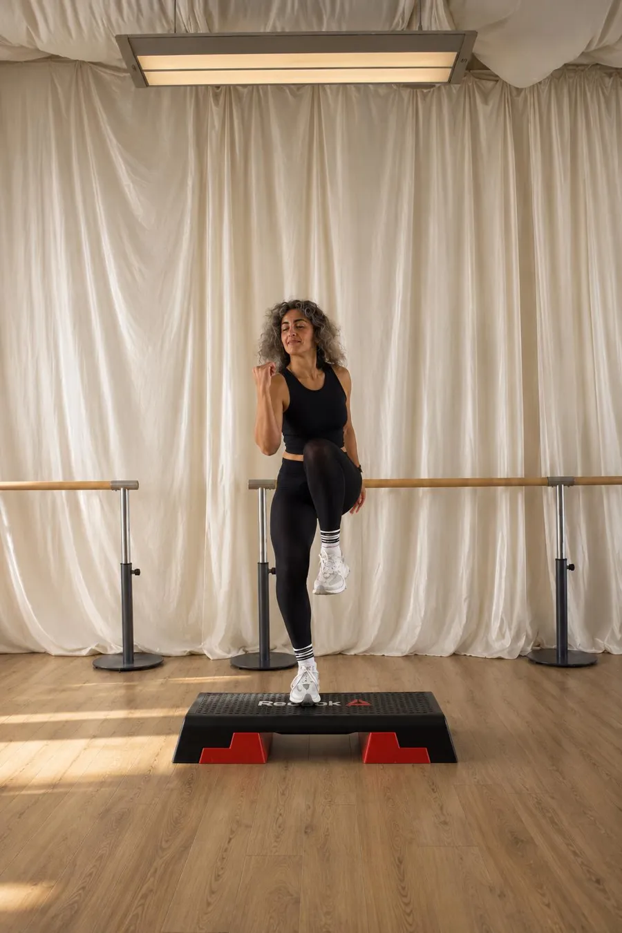 A smiling instructor stepping up onto a step platform during a step class at URWAY